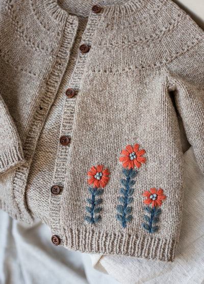 Daisy: trio of orange-petaled flowers with blue stems embroidered on beige knit cardigan.