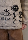 Millepora: leaf-like embroidery in organic patterns near hem of brown knit sweater.