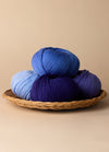 Three colorful balls of superwash merino wool yarn in a wicker basket, ideal for baby and children's projects.