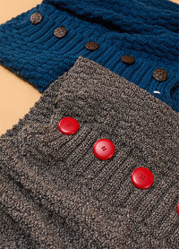 Close-up of two knitted scarves. The gray scarf has red buttons, while the blue one features dark brown buttons. Displayed on a beige background.