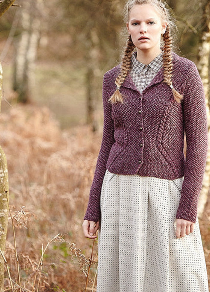 Person wearing the Eriskay Jacket, a purple textured knit with front buttons, paired with a polka dot dress in a natural outdoor setting.