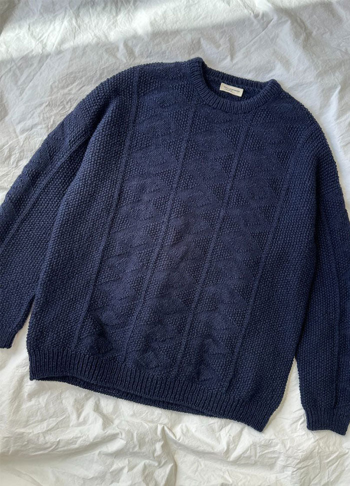 Flat lay of the Esther Sweater in navy blue textured knit with geometric pattern, round neckline, and ribbed cuffs, displayed on a white fabric background.