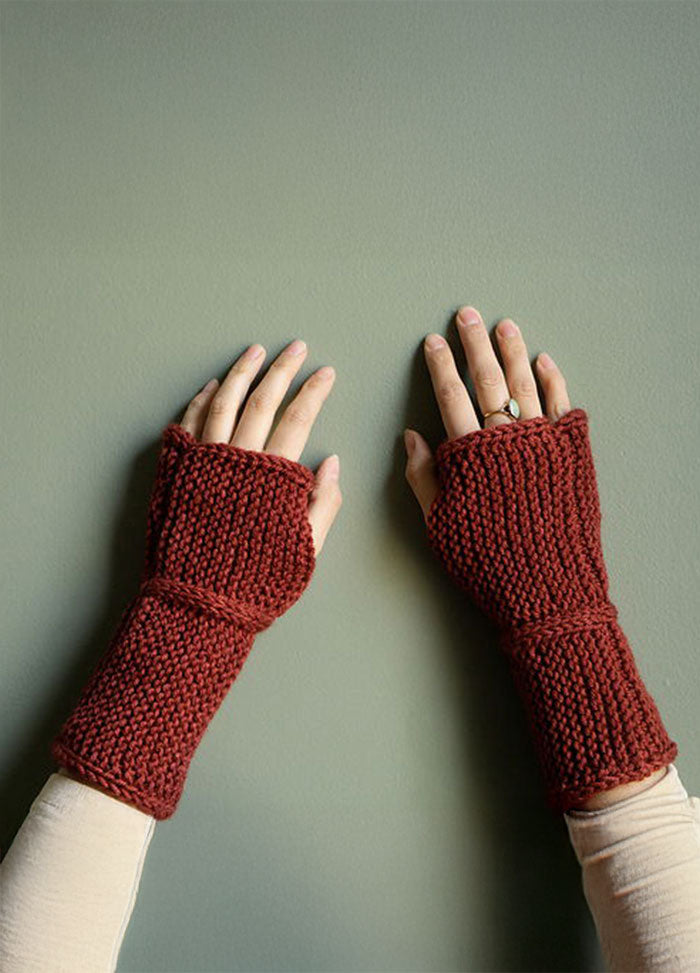 Everyday Handwarmers in deep red, hand-knit and fingerless, worn on hands against a green background.