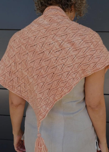 Woman wearing a delicate pink knitted shawl with an intricate lacy pattern and a tassel. The tone is warm and cozy, with a sophisticated touch.