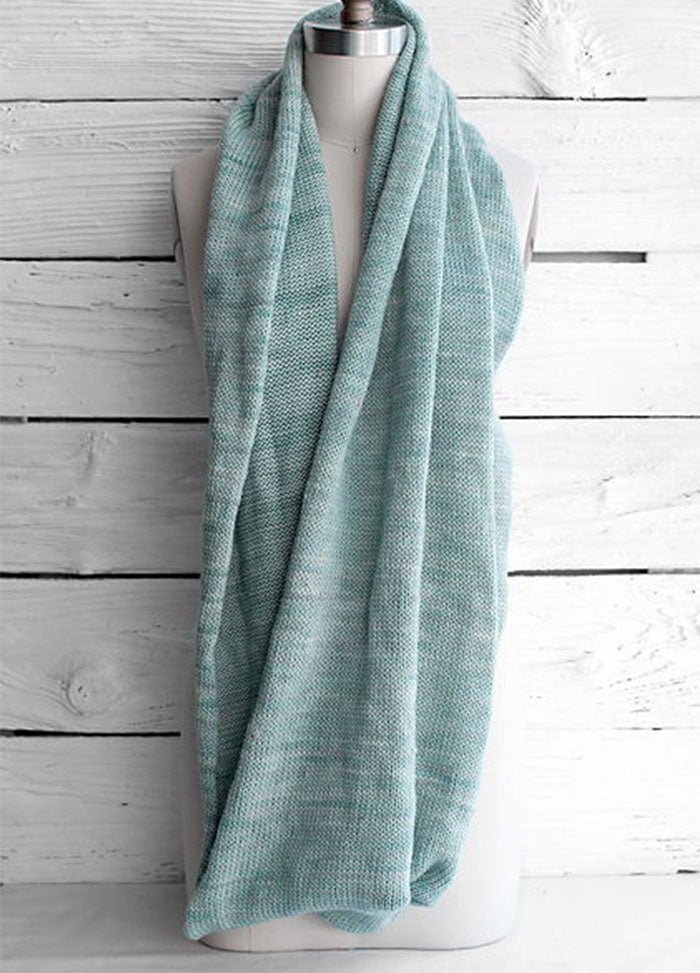 Fino Circle Scarf in light blue, featuring a soft, textured knit, styled in a loose loop around a mannequin’s neck, set against a white wooden background.