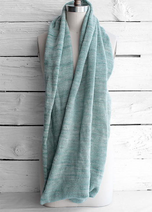 Fino Circle Scarf in light blue, featuring a soft, textured knit, styled in a loose loop around a mannequin’s neck, set against a white wooden background.
