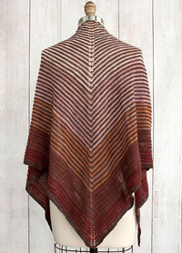 Fino Shadow Shawl on a mannequin, featuring a gradient of brown, orange, and red stripes in a V-shaped pattern, displayed against a wooden background.