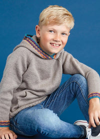 A smiling boy with blonde hair sits casually against a blue background. He's wearing a gray knit hoodie with colorful trim and blue jeans, exuding a cheerful vibe.