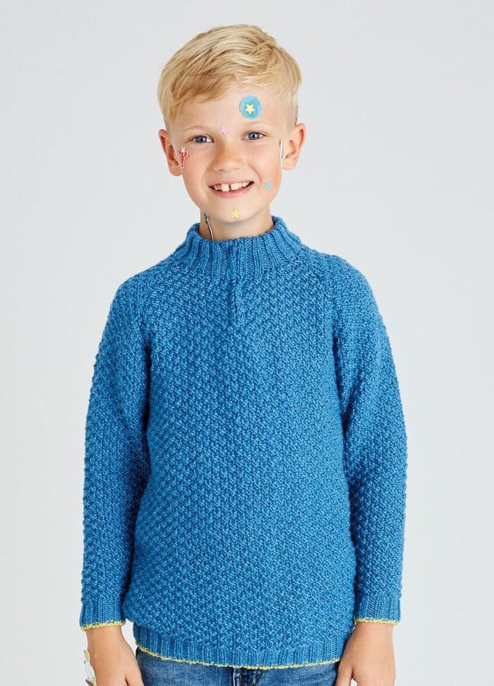Smiling young boy with blond hair wears a textured blue sweater. His face has colorful star stickers, creating a playful, cheerful vibe.