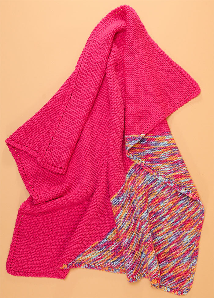 Florence Blanket in bright pink with a reverse side featuring a geometric multicolored pattern in blue, yellow, and white.
