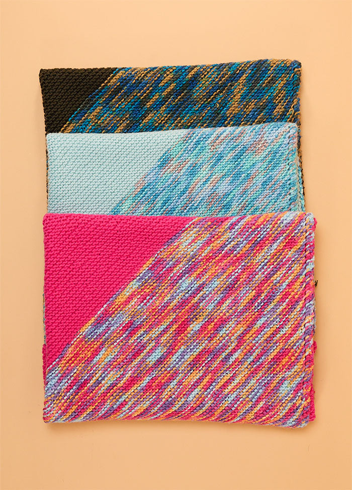 Stacked Florence Blankets in black, light blue, and bright pink, each with distinct multicolored patterns and trims.
