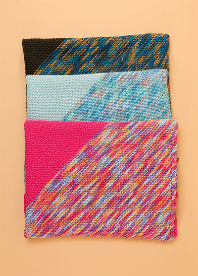 Stacked Florence Blankets in black, light blue, and bright pink, each with distinct multicolored patterns and trims.