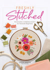 Cover of “Freshly Stitched: Modern Embroidery for Absolute Beginners” by Celeste Johnston of Lemon Made Shop. Features an embroidery hoop with a floral design, colorful threads on bobbins, ornate scissors, and folded fabric, highlighting the book’s beginner-friendly approach to modern embroidery.
