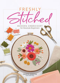 Cover of “Freshly Stitched: Modern Embroidery for Absolute Beginners” by Celeste Johnston of Lemon Made Shop. Features an embroidery hoop with a floral design, colorful threads on bobbins, ornate scissors, and folded fabric, highlighting the book’s beginner-friendly approach to modern embroidery.