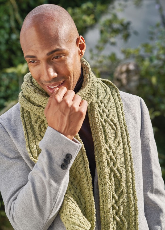 A man wearing a thick, green knitted scarf with a textured pattern, draped comfortably around his neck.