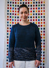 Hand-knit Galaxy Sweater in deep blue with light speckles on lower body and sleeves, shown on a model before a vibrant grid backdrop.