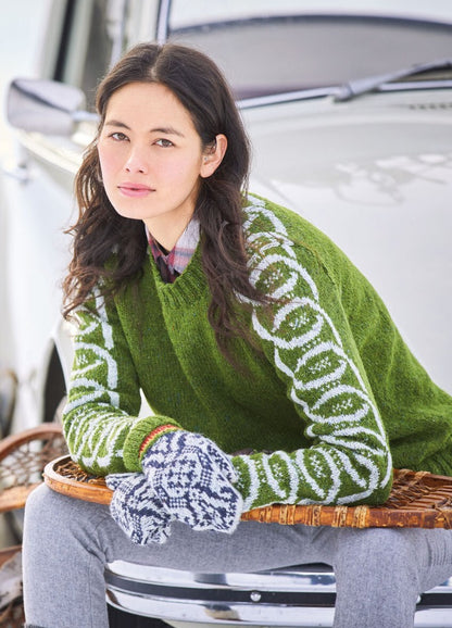 Young woman in a green sweater with patterned sleeves leans against a car, wearing gray mittens and gray pants, exuding a relaxed and thoughtful vibe.