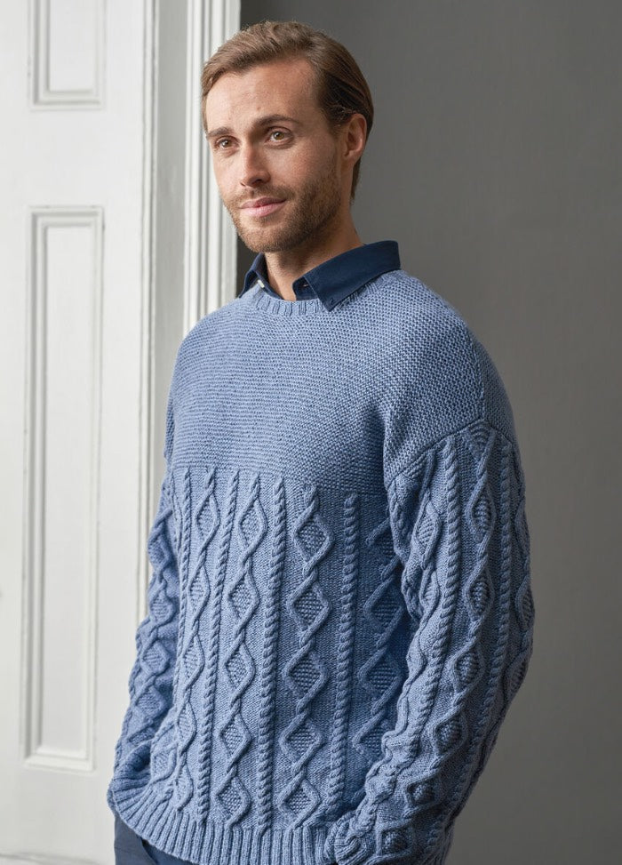 A man wearing a textured blue knit sweater and matching blue pants, standing confidently with a neutral background.