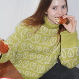 A woman enjoying a sandwich while wearing the Heart Together Sweater, featuring a boxy fit and wide sleeves.