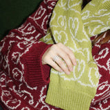 A woman showcases a boxy-fit green and red sweater with wide sleeves and a turtleneck, paired with the green sweater.