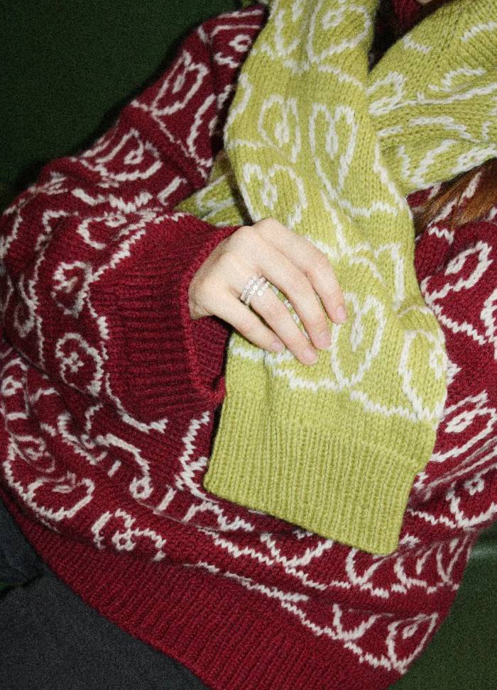 A person wearing a red sweater with white patterns holding a yellow sweater with an abstract design.