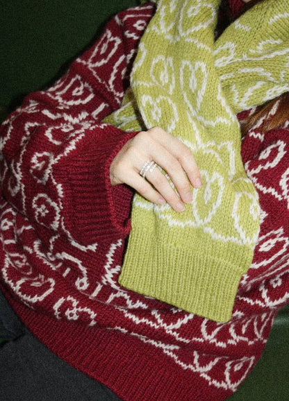 A person wearing a red sweater with white patterns holding a yellow sweater with an abstract design.