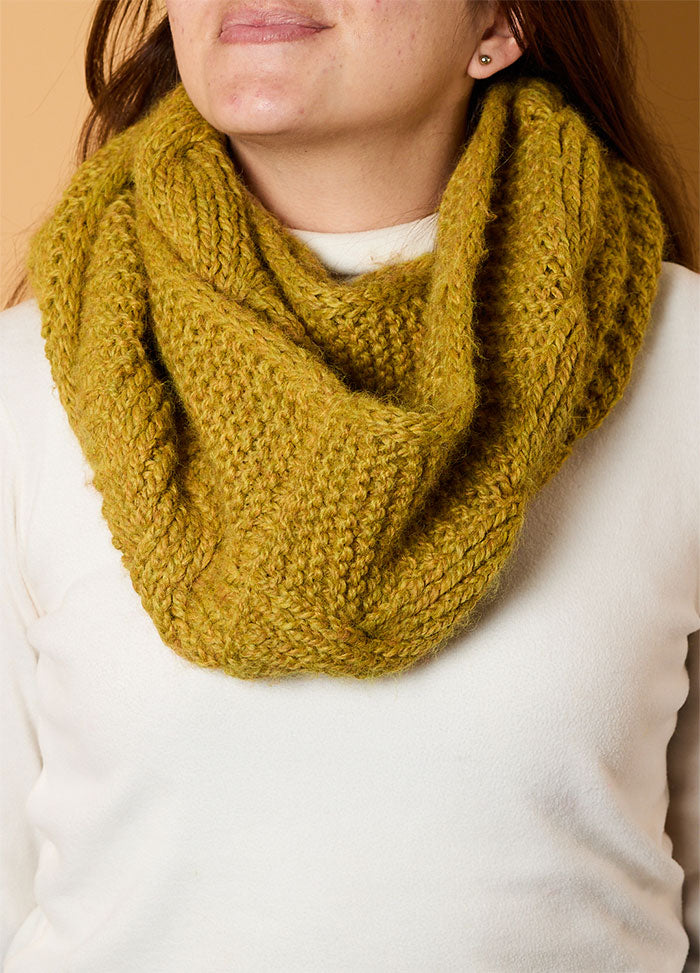Person wearing the Honey Cable Cowl, a chunky mustard yellow knitted cowl with a wide cable design, styled over a white top.