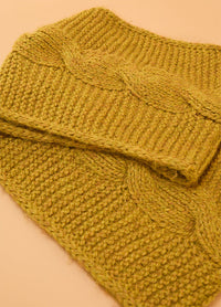 Close-up of the Honey Cable Cowl, a hand-knitted mustard yellow cowl featuring a wide braided cable pattern against a textured stitch background.