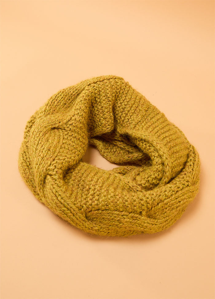 Honey Cable Cowl arranged in a loose circular shape, showing its chunky mustard yellow knit with wide braided cables and textured stitches on a beige background.