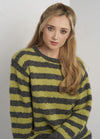 Woman with long blonde hair wearing a fuzzy green and gray striped sweater. She sits against a plain white background, conveying a calm and relaxed tone.
