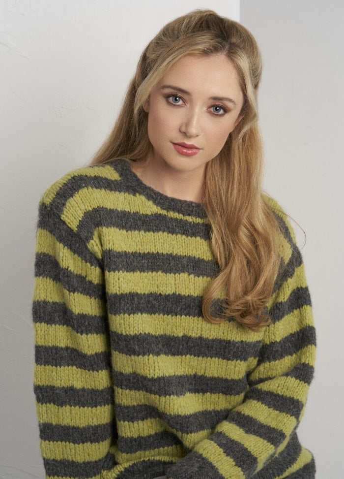 Woman with long blonde hair wearing a fuzzy green and gray striped sweater. She sits against a plain white background, conveying a calm and relaxed tone.