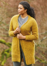 Woman in a mustard yellow cardigan stands outdoors, gazing sideways with serenity. The background features blurred trees, conveying a calm autumn vibe.