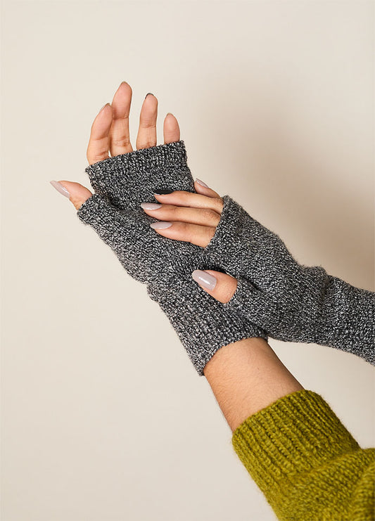 Pair of gray hand-knitted fingerless gloves covering wrists and palms, worn with a green sweater – practical and stylish accessory for cooler weather.