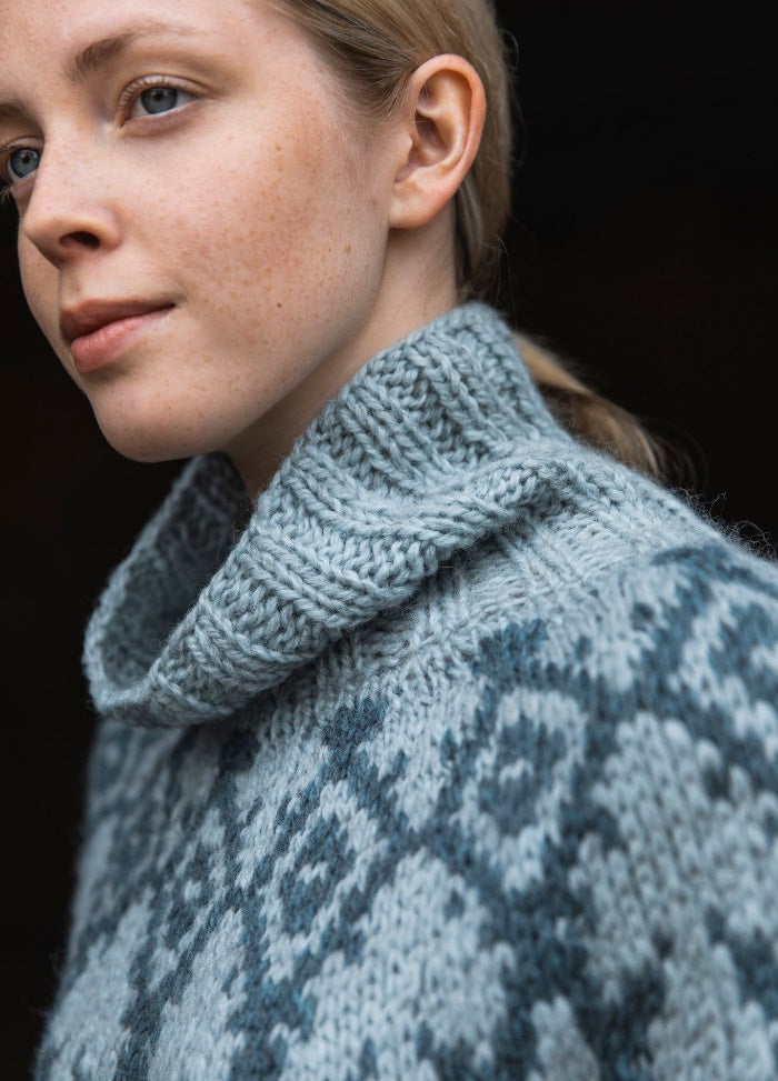 Iku-Turso Sweater: high-collared knit with intricate blue and gray geometric patterns, shown in a close-up highlighting texture and detail.