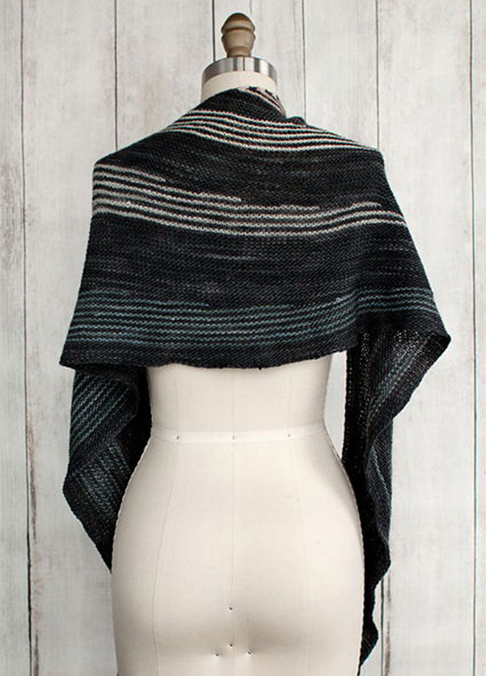 Incremento Shawl on a mannequin, featuring diagonal stripes on a dark base, displayed against a wooden background.