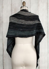Incremento Shawl on a mannequin, featuring diagonal stripes on a dark base, displayed against a wooden background.