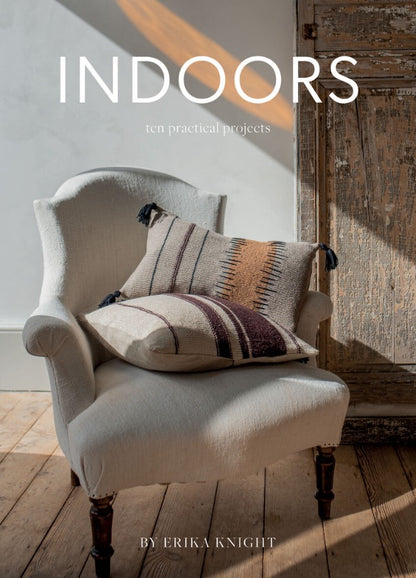 A cozy armchair with patterned cushions sits on a wooden floor, bathed in warm sunlight. The background shows a rustic wooden door.