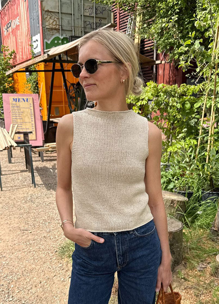 Woman wearing the Ivy Top in sleeveless beige knit with high neckline, styled with blue jeans in an outdoor setting with greenery.