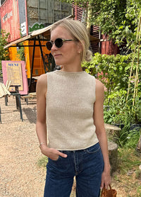 Woman wearing the Ivy Top in sleeveless beige knit with high neckline, styled with blue jeans in an outdoor setting with greenery.