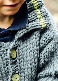 Jesse Cardigan: Close-up of a thick, hand-knitted gray cardigan with large buttons and green stitching near the collar, worn over a dark blue shirt.