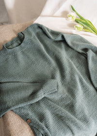 A teal knit sweater is laid out on a beige surface, accompanied by two white tulips on a light fabric background, creating a cozy and serene atmosphere.