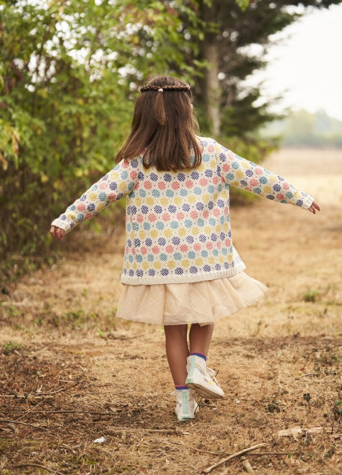 A young girl in a colorful sweater and fluffy skirt walks away down a forest path. Her arms are outstretched, conveying a sense of freedom and joy.