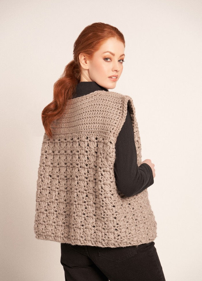 Chunky crochet gilet with tie fastening and textured stitches, worn over a long-sleeve top.