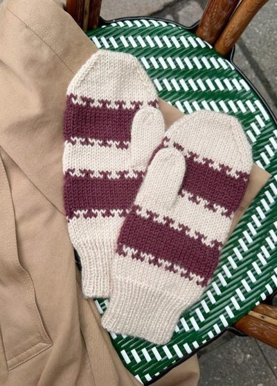 Cozy knit mittens with burgundy and cream stripes, lie on a tan jacket draped over a woven green and white chair.