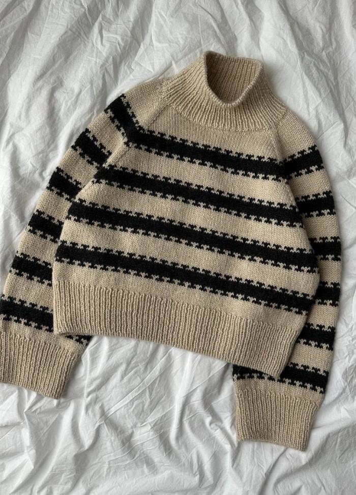 A cozy, beige knit sweater with black horizontal stripes and a high collar, laid on a rumpled white fabric, conveying warmth and comfort.