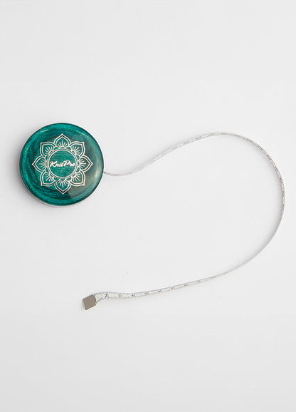  Teal wooden tape measure with a green button, white cord, and gold lotus design, part of the Mindful Collection accessories.