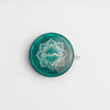  A green and white button on a teal tape measure with a lotus design, complementing the Mindful Collection's accessories.
