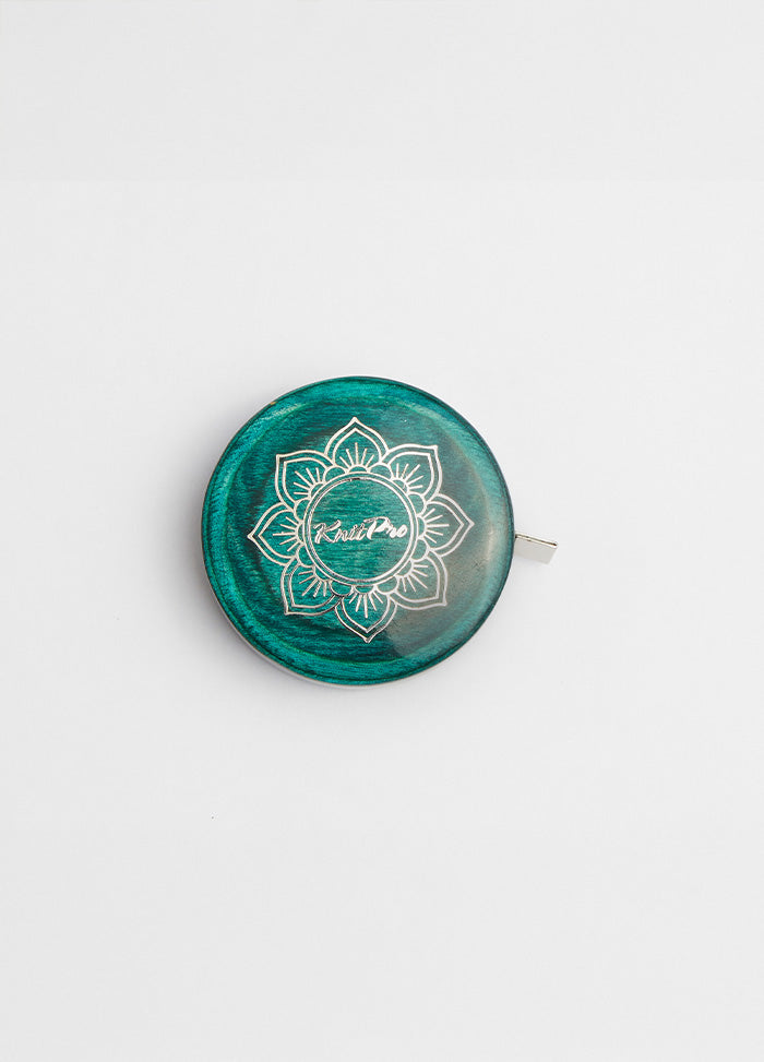  A green and white button on a teal tape measure with a lotus design, complementing the Mindful Collection's accessories.