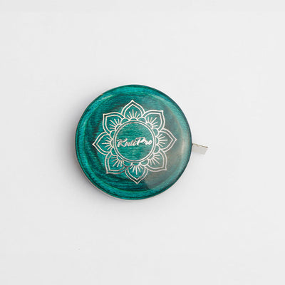  A green and white button on a teal tape measure with a lotus design, complementing the Mindful Collection's accessories.