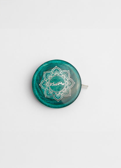  A green and white button on a teal tape measure with a lotus design, complementing the Mindful Collection's accessories.